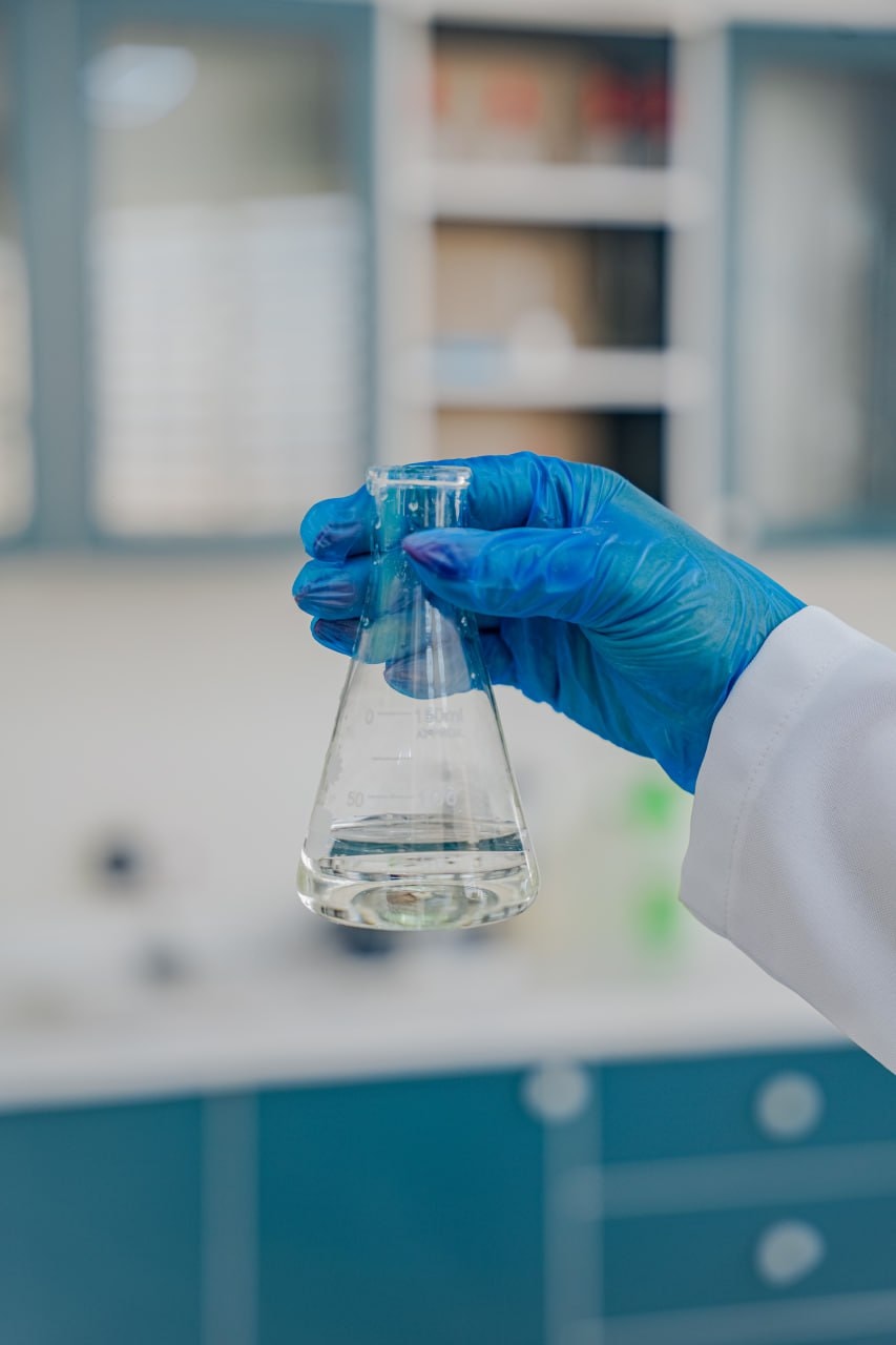 A gloved hand holding a flask of clear solution in the laboratory